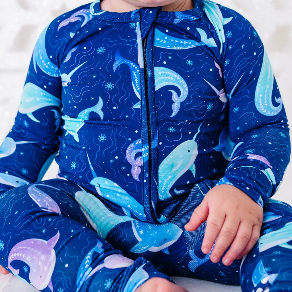 Close up of the front zipper and chest of a zip up baby pajama in a royal blue print of blue and lavender narwhals.